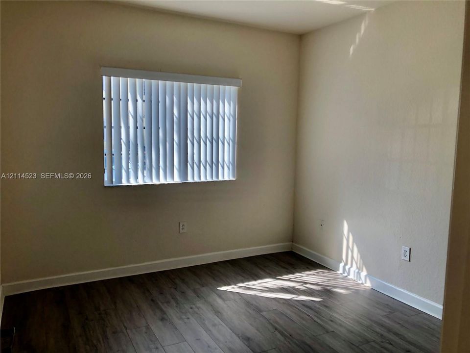 Neutral-toned interior space featuring wood-finish flooring, light-colored walls, and a window equipped with vertical blinds