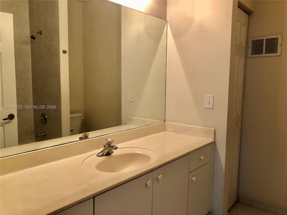 Bathroom vanity featuring a solid surface countertop with integrated basin, chrome finish faucet, white cabinetry, and a full-width wall mirror