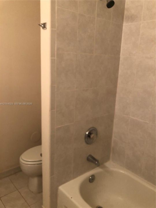 Full-height wall tile surrounding a white tub-shower combination with chrome fixtures and a porcelain toilet