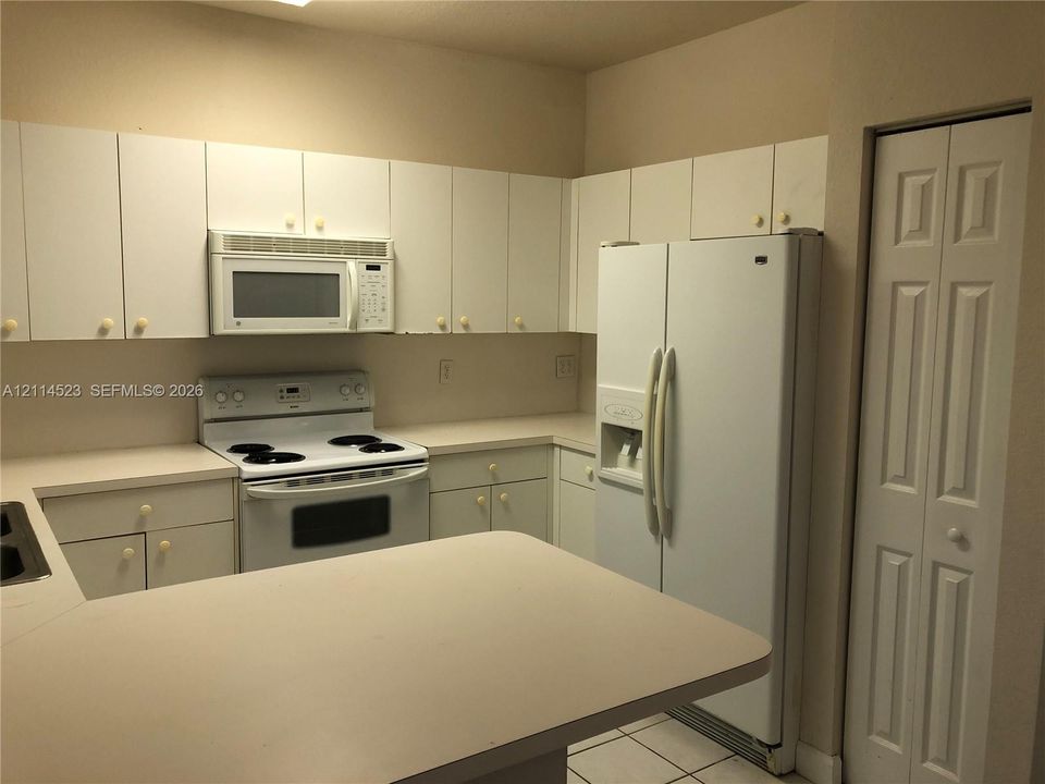 Kitchen featuring white cabinetry, solid-surface countertops, integrated microwave, range, and floor-to-ceiling bi-fold door pantry