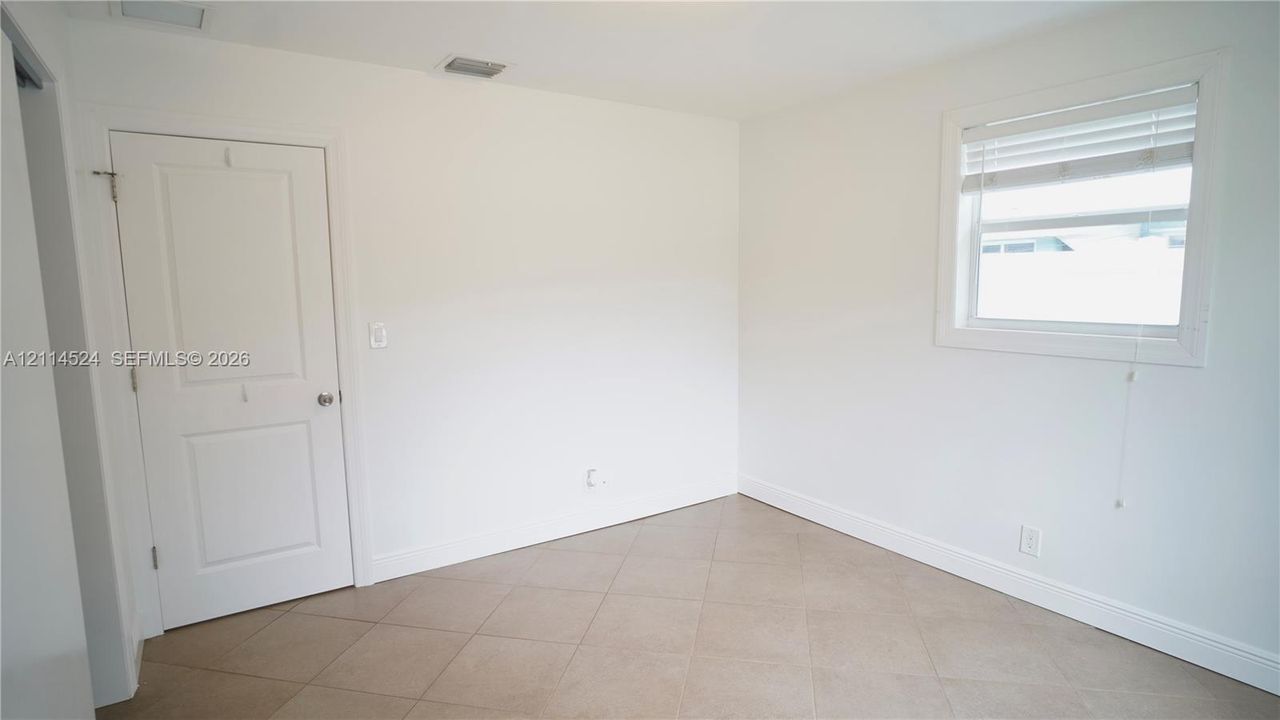 Neutral room interior featuring large-format ceramic tile flooring, a two-panel interior door with brushed metal hardware, and a single-hung window with fitted blinds