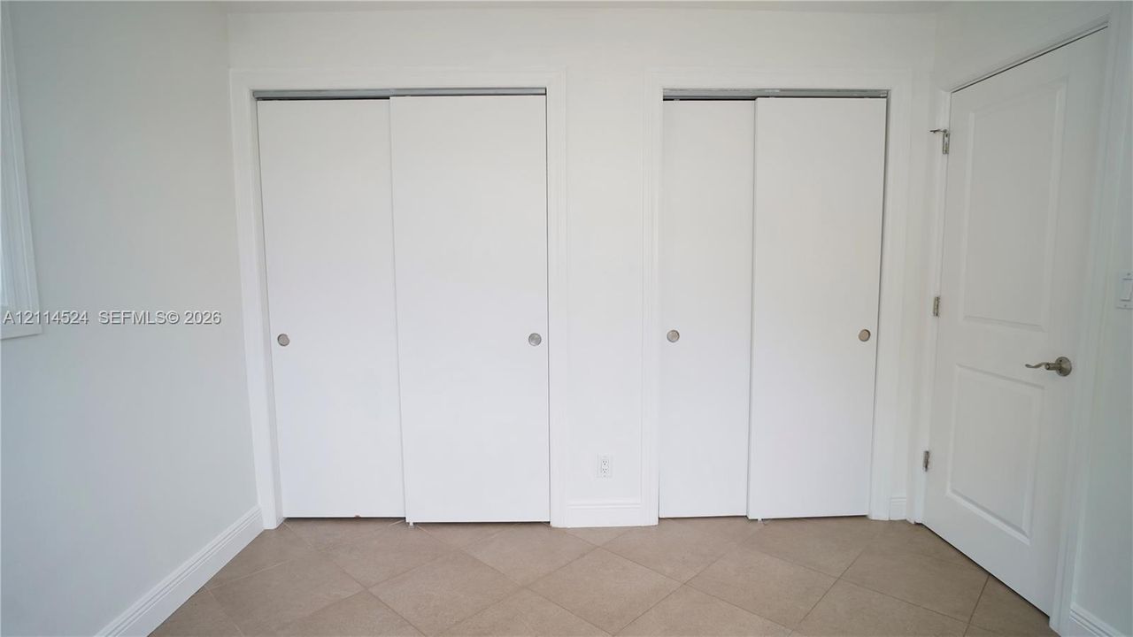 Dual floor-to-ceiling closets with sliding doors, neutral ceramic tile flooring, and a solid-core interior swing door