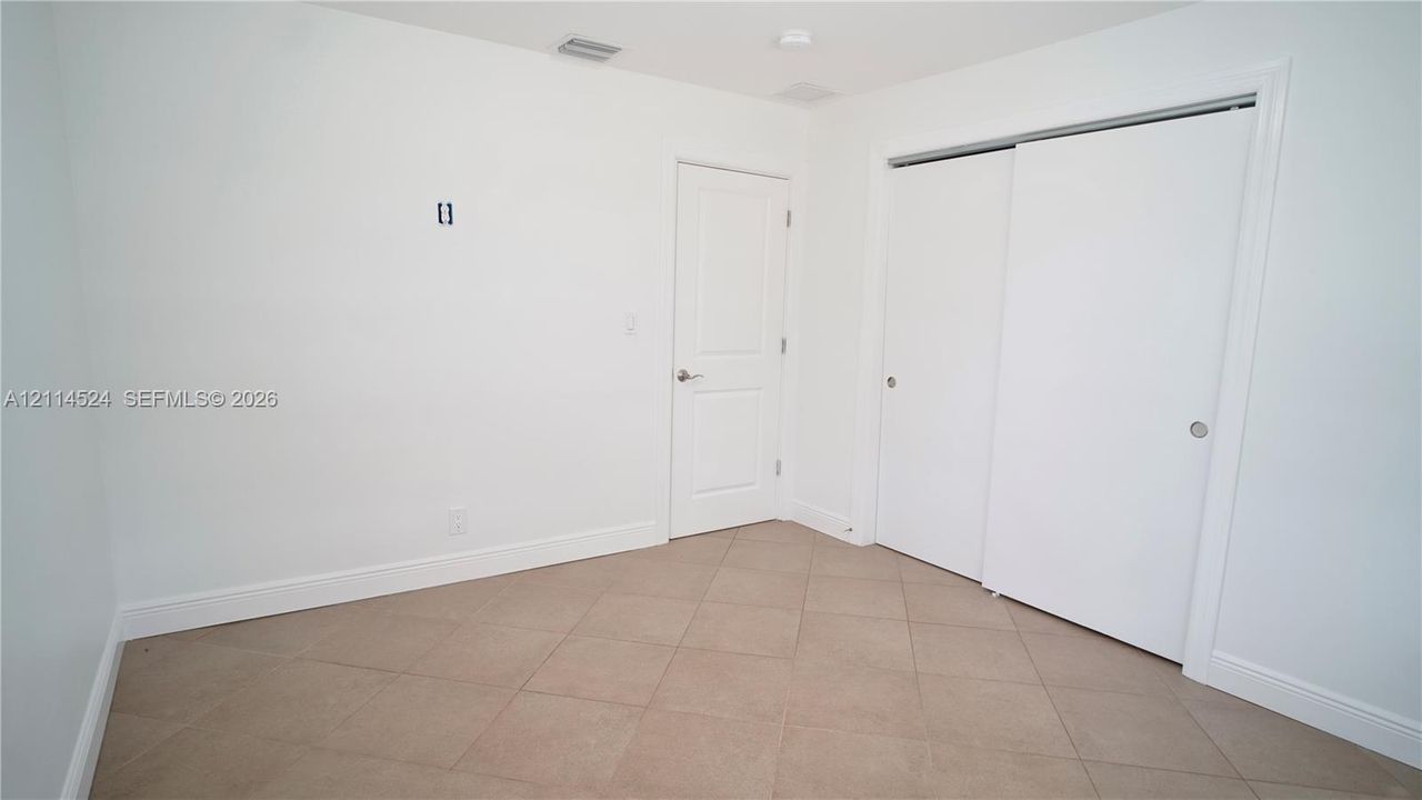Neutral-toned tile flooring, solid-core interior door, and dual sliding-door closet with clean white finishes