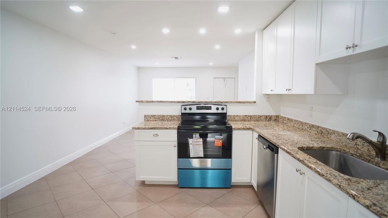 Kitchen featuring white shaker-style cabinetry, stone-patterned countertops, a stainless steel freestanding range, a stainless steel dishwasher, and tiled flooring