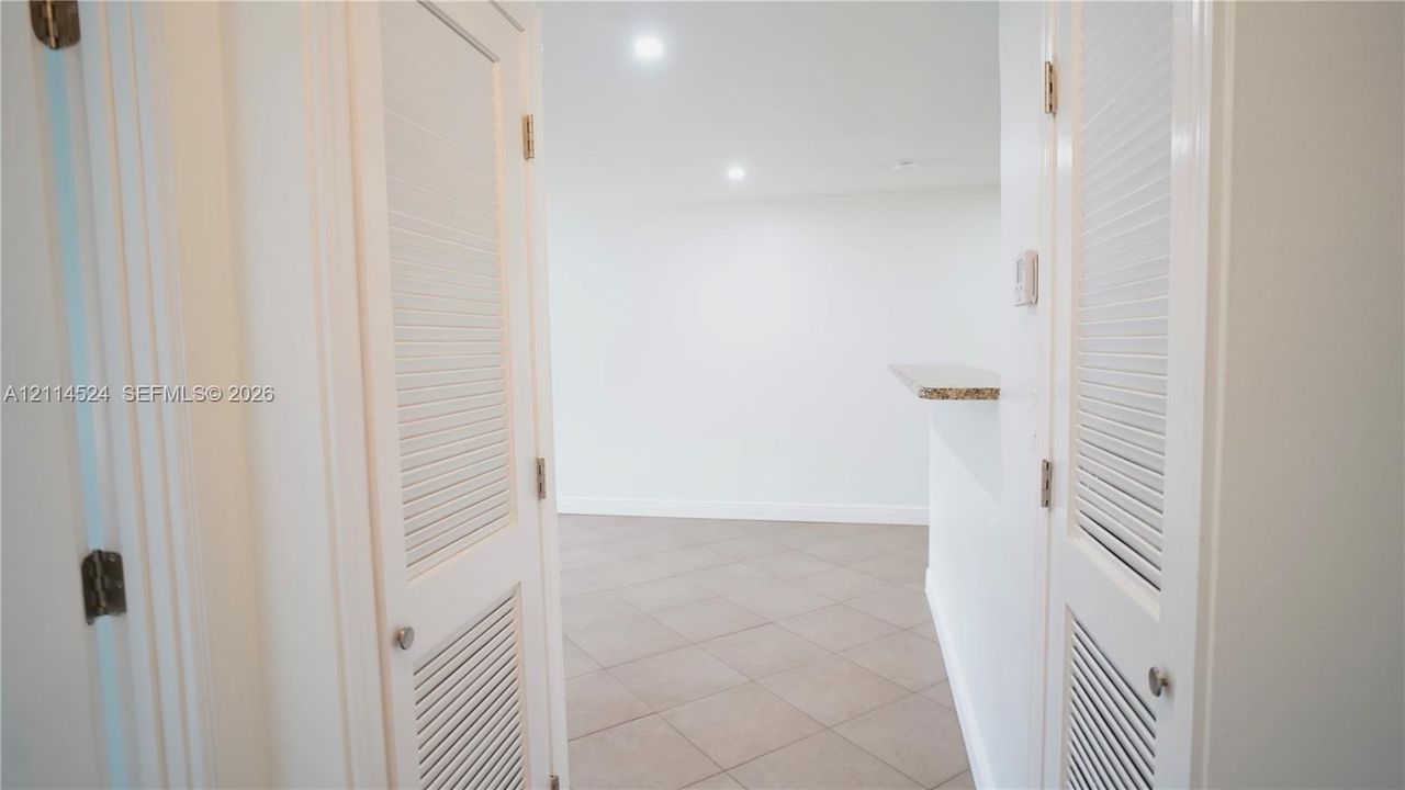 Dual louvered-door closets, neutral-tone tile flooring, recessed lighting, and a stone-surface pass-through counter