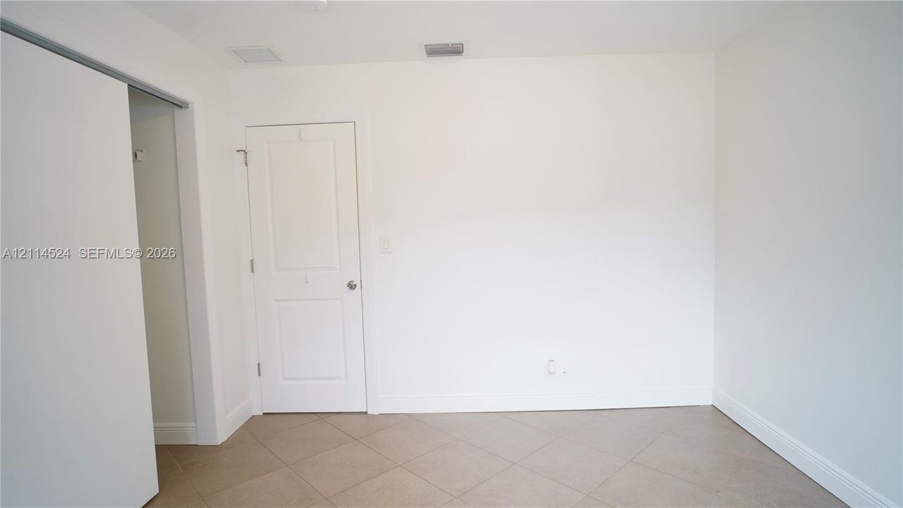 Interior space featuring large-format neutral tile flooring, white walls, a solid-core interior door with satin nickel hardware, and a sliding door closet