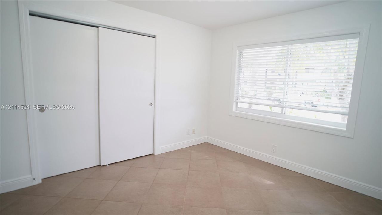 Neutral-toned tile flooring, white sliding closet doors, and a window with horizontal blinds