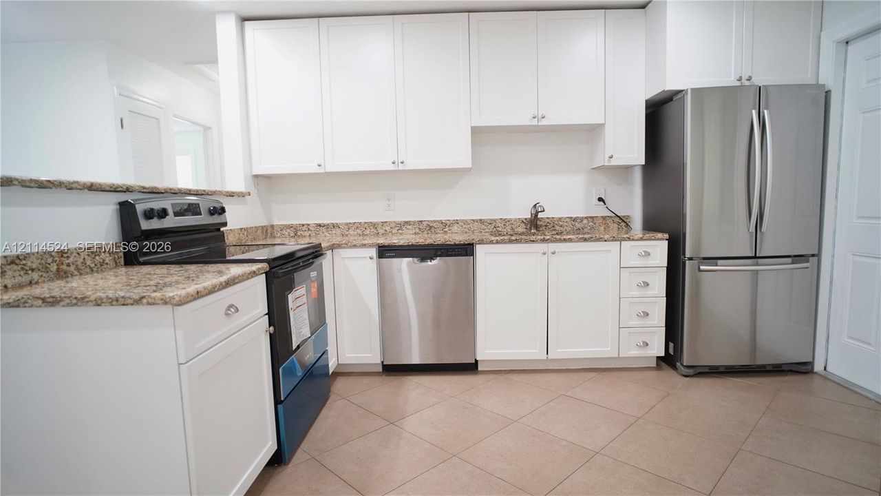 Kitchen featuring white shaker-style cabinetry, stone-patterned countertops, a stainless steel dishwasher, a stainless steel refrigerator, and tiled flooring