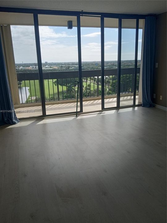Floor-to-ceiling sliding glass panels, light-tone wood-finish flooring, and a private balcony with metal railings overlooking the landscape