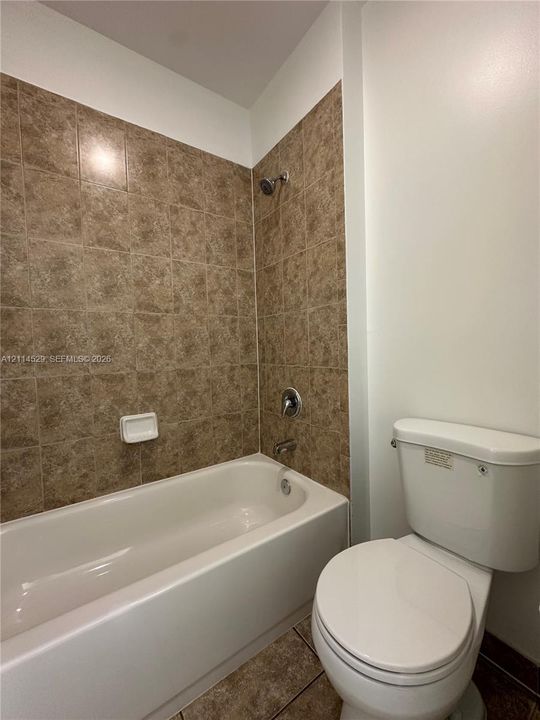 Bathtub featuring full-height textured tile surround, built-in soap dish, and metal shower fixtures