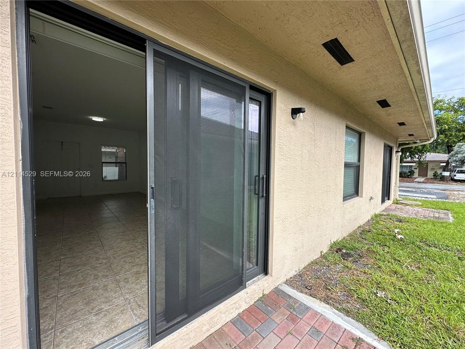 Stucco exterior with recessed lighting, sliding glass door featuring a screen, and a paved brick patio