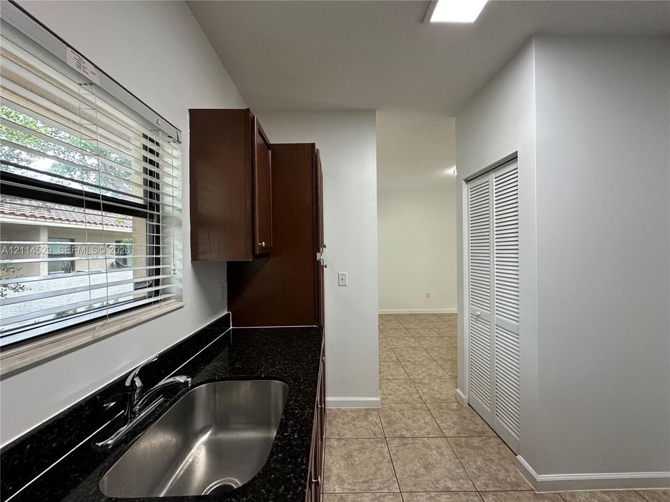 Dark-toned cabinetry featuring a high-contrast countertop, integrated stainless steel sink with a metallic faucet, horizontal window blinds, and louvered bifold closet doors