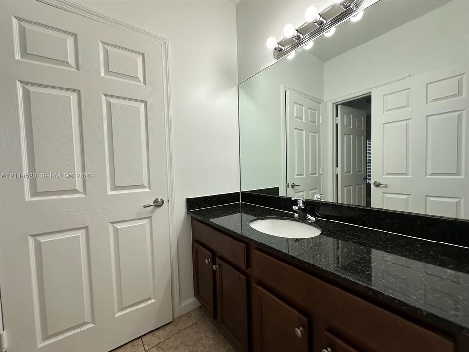 Bathroom vanity featuring a dark stone countertop, integrated oval sink, chrome faucet, shaker-style wood cabinetry, and a full-width wall mirror with a multi-bulb light fixture