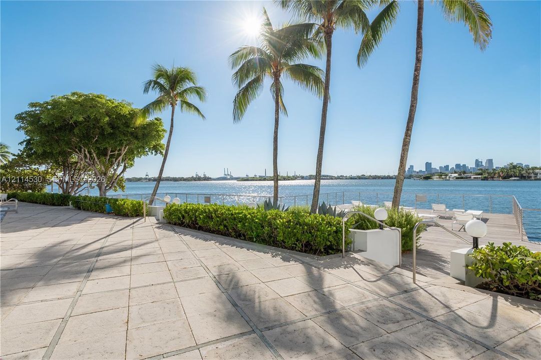 Waterfront terrace featuring stone paver flooring, perimeter metal railings, mature palm trees, and manicured shrubbery