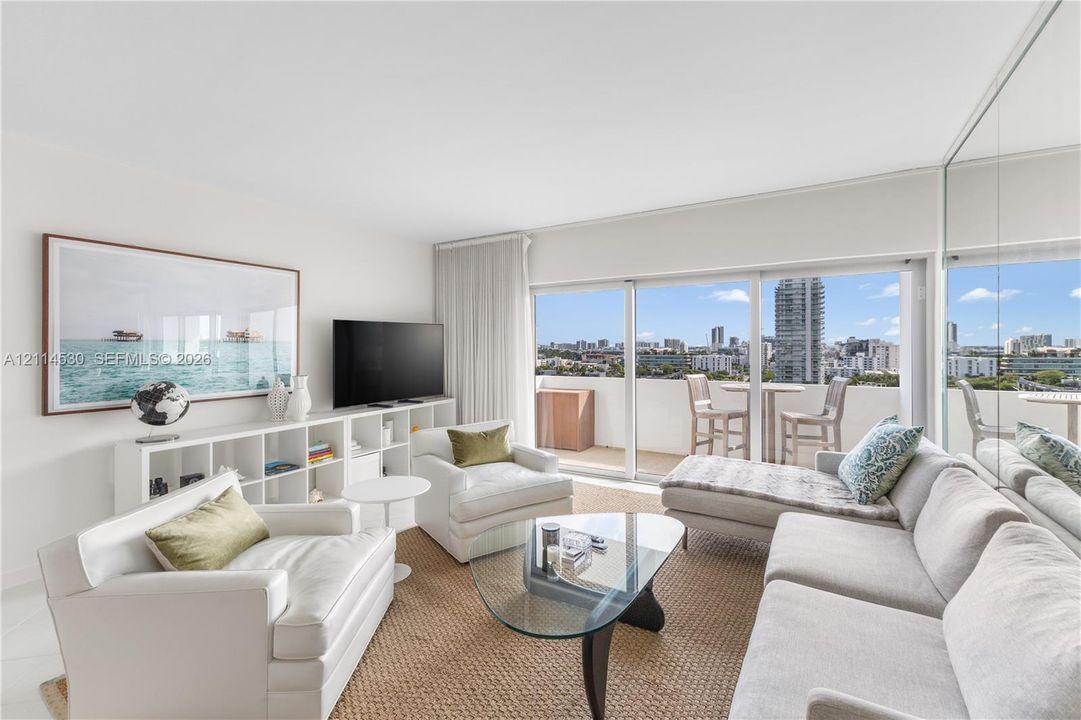 Living area featuring full-height glass sliding doors, private balcony, floor-to-ceiling mirrored wall, and built-in shelving unit