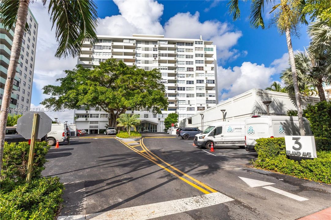Multi-story mid-century architecture featuring private balconies, expansive asphalt drive, mature canopy trees, and landscaped grounds