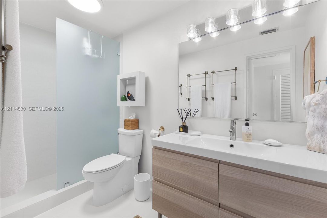 Bathroom featuring a floating vanity with a seamless integrated sink, wood-finish cabinetry, a large wall-mounted mirror, a walk-in shower with a frosted glass panel, and built-in recessed wall shelving