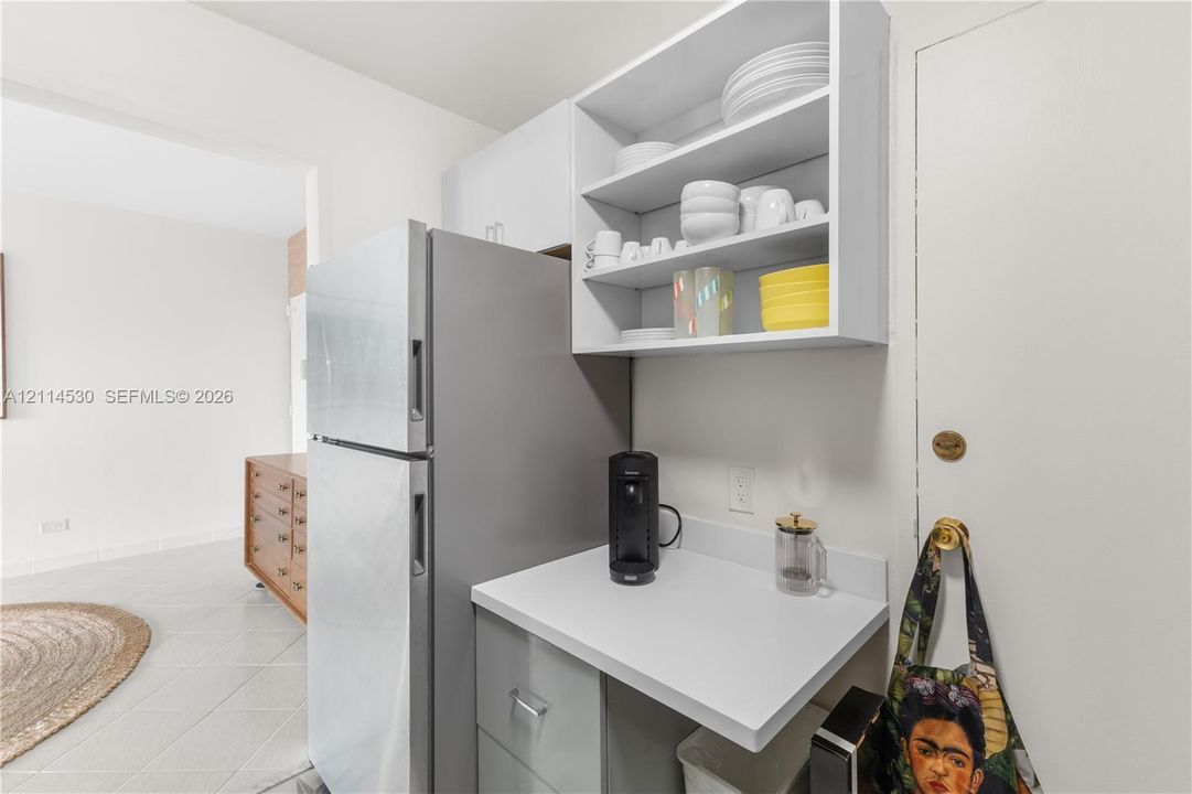 Kitchenette featuring matte-finish cabinetry, white solid-surface countertop, stainless steel refrigerator, and open shelving