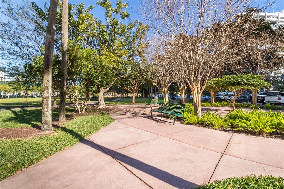 Outdoor grounds featuring concrete walkways, manicured lawn, established trees, and metal bench seating