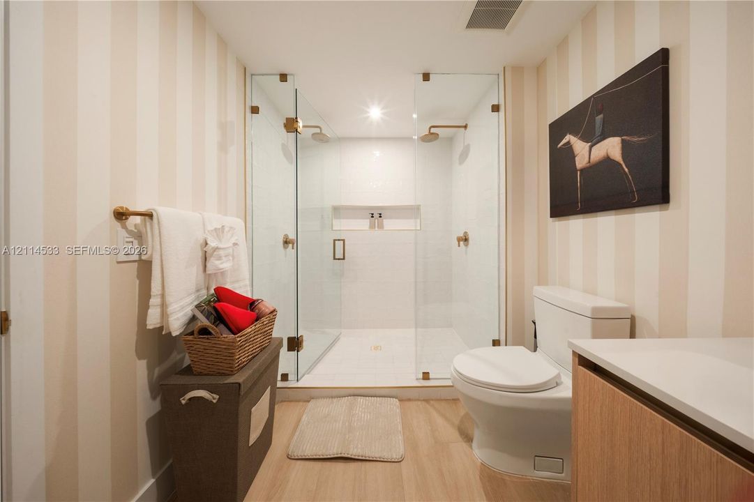 Walk-in shower featuring a frameless glass enclosure, dual showerheads, and an integrated wall niche, complemented by wood-finish flooring and brass-finish hardware