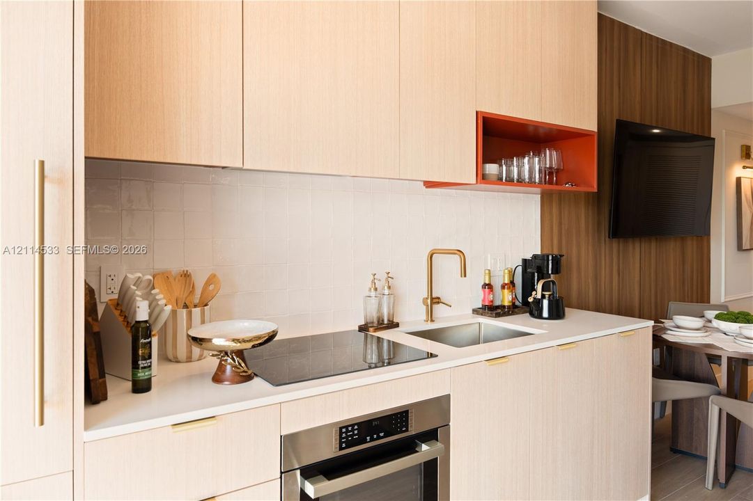 Modern kitchenette featuring light wood-finish cabinetry, white tile backsplash, a metallic faucet, a built-in cooktop, and a contrasting open-shelf accent