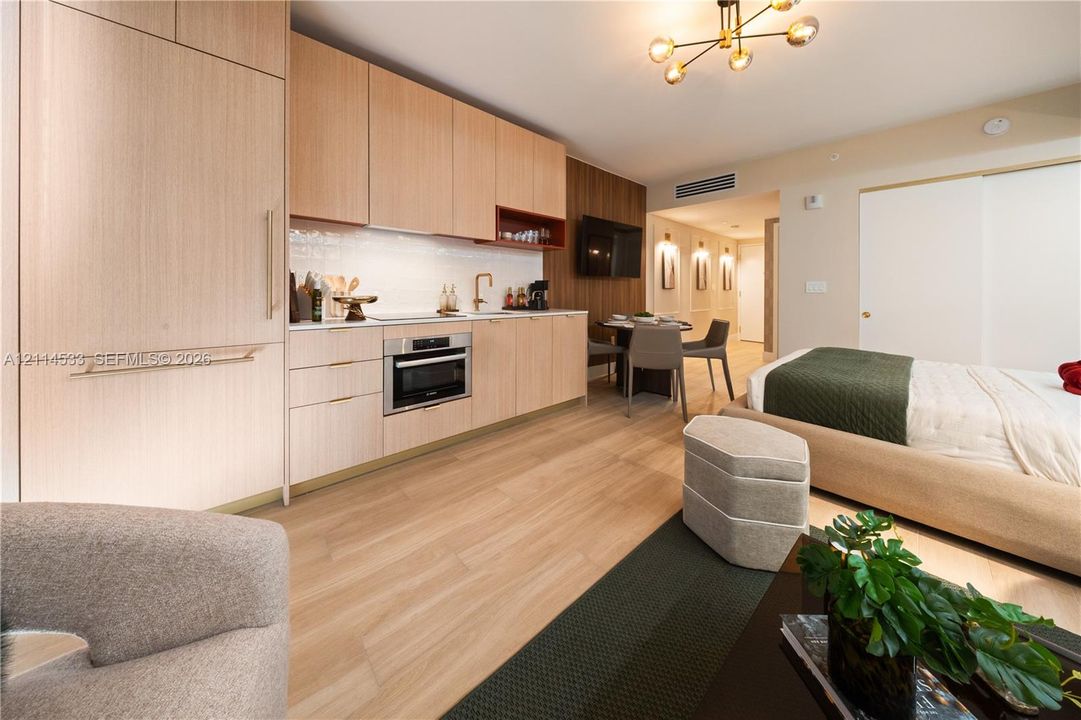 Modern kitchen featuring light wood-finish cabinetry, integrated appliances, gold-tone hardware, wood-finish flooring, and a multi-arm metallic light fixture