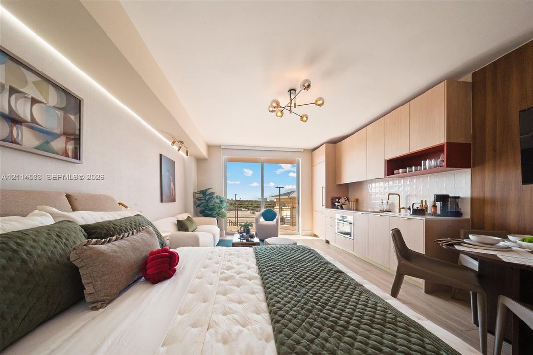 Kitchenette featuring light wood-finish cabinetry, built-in appliances, recessed under-cabinet lighting, and a modern multi-bulb ceiling fixture, complemented by sliding glass doors leading to an exterior balcony