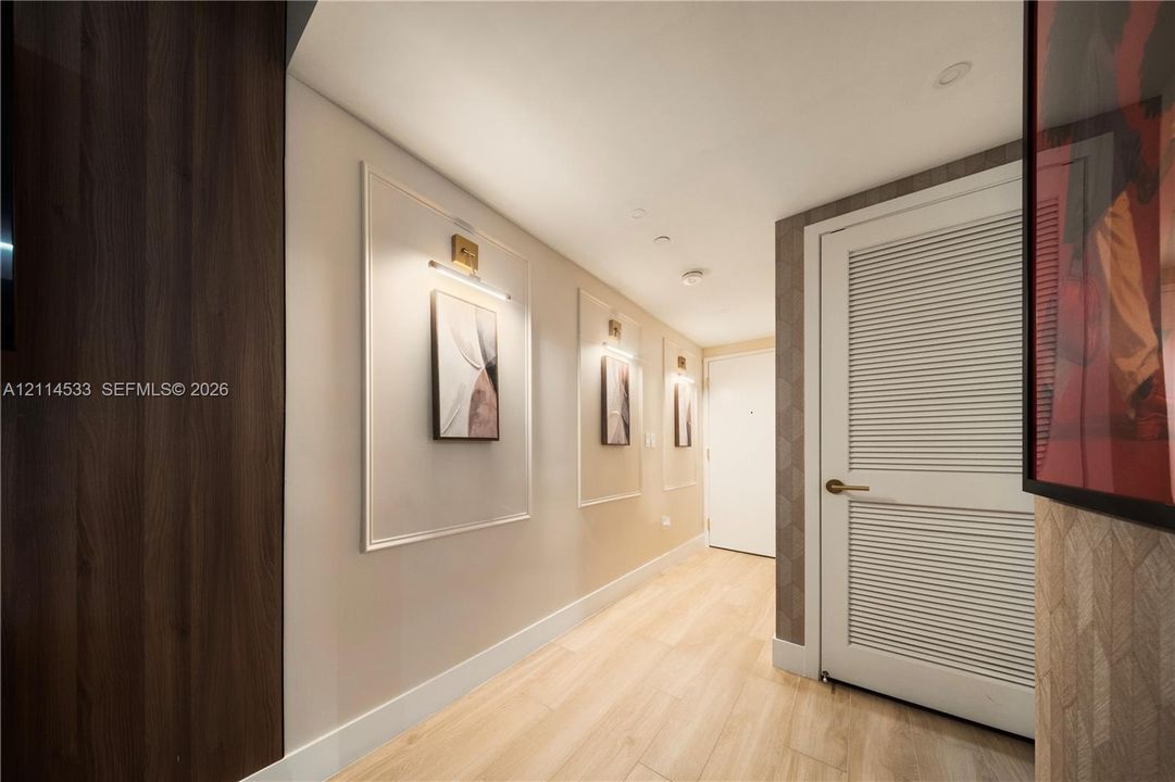 Hallway featuring wood-finish flooring, wall paneling with decorative molding, recessed lighting, and a louvered door