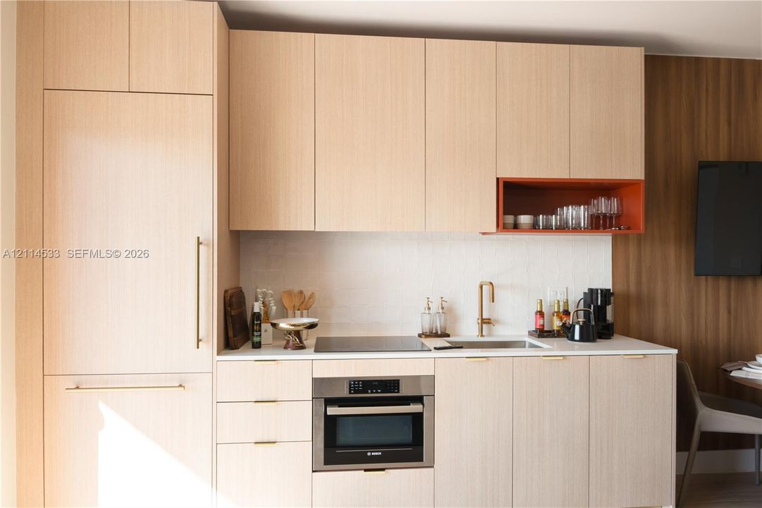 Flat-panel wood cabinetry with integrated refrigerator, built-in stainless steel oven, induction cooktop, contrasting open shelving, and brushed gold hardware