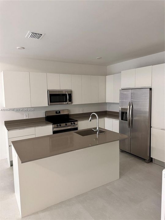 Kitchen featuring white flat-panel cabinetry, a central island with a solid surface countertop, stainless steel appliances, and a double-door refrigerator