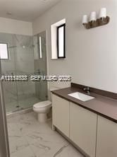 Bathroom featuring a walk-in shower with frameless glass enclosure, vanity with integrated basin, stone-finish countertop, and three-light wall-mounted fixture