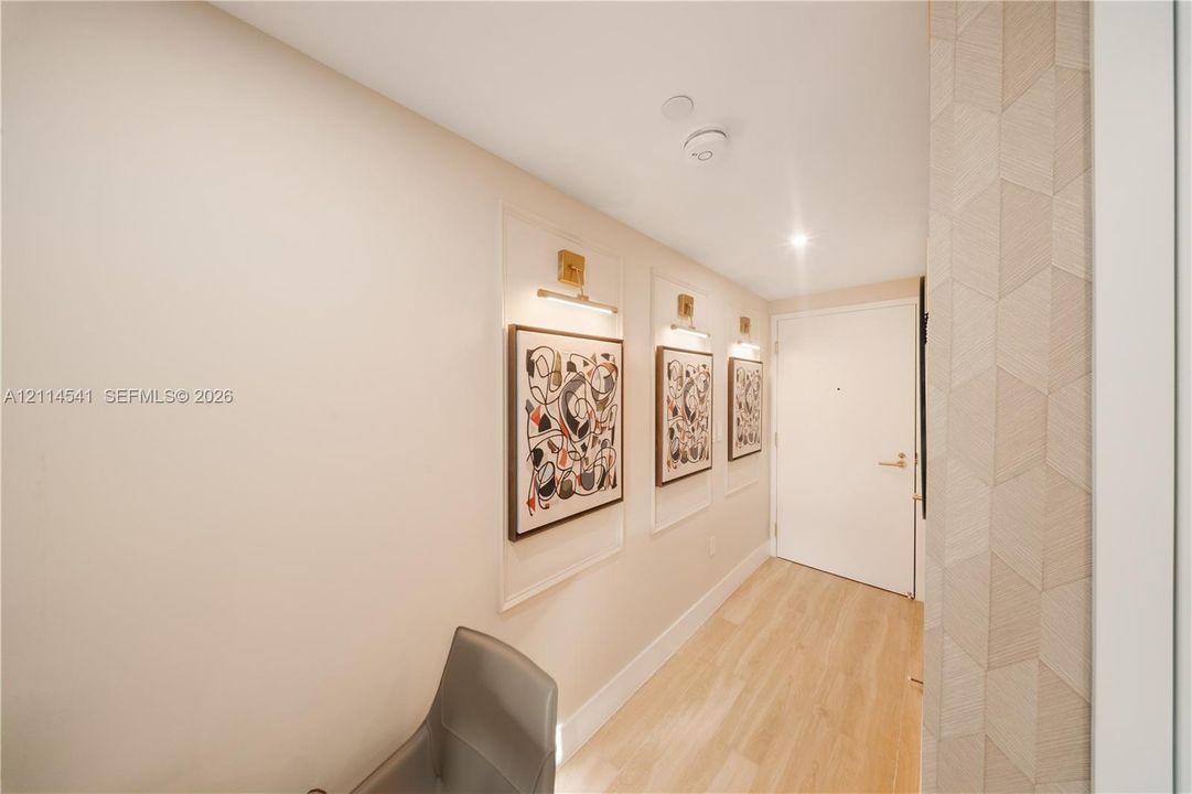 Entryway featuring wood-finish flooring, recessed wall panels with integrated picture lighting, and geometric patterned wall texture
