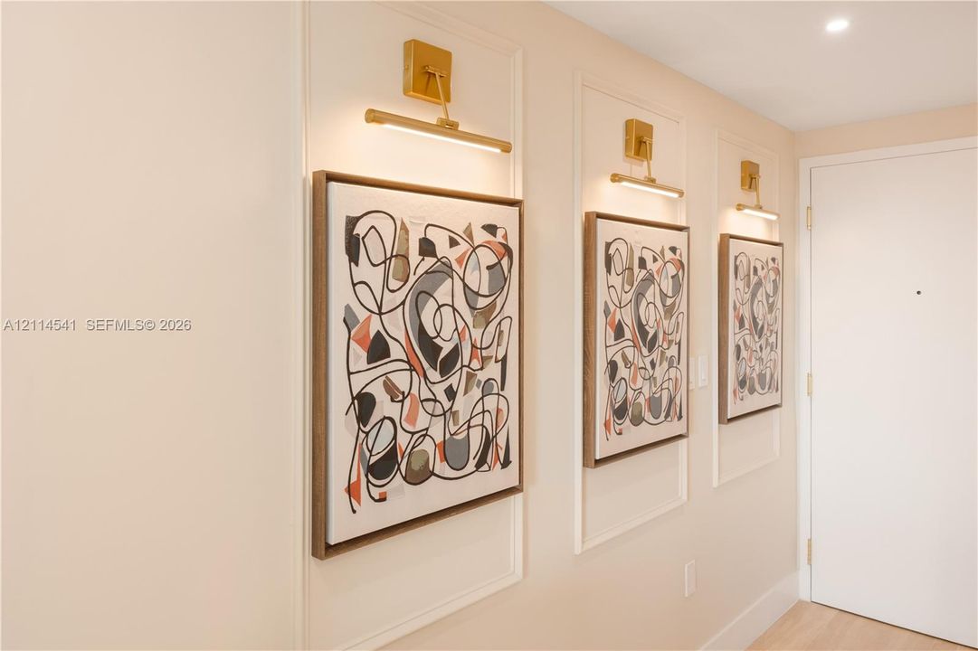 Wall-mounted brass picture lighting, custom wall molding, and neutral wall finish