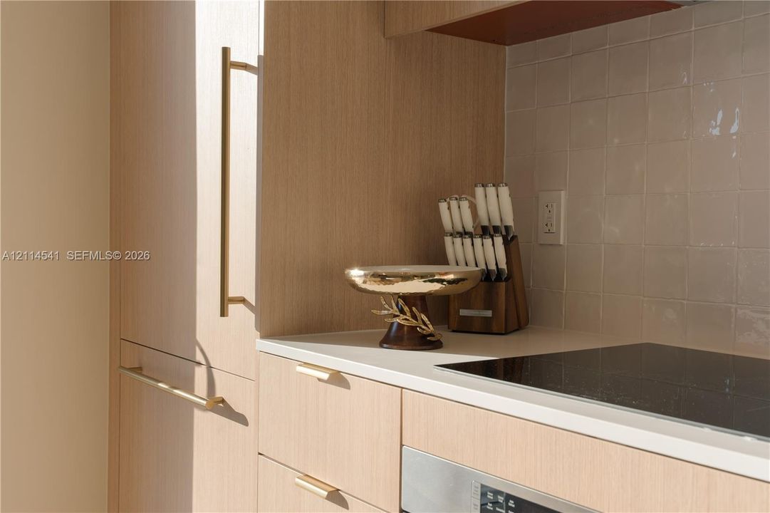 Light-finish cabinetry with metallic pulls, white solid-surface countertop, and square-tile backsplash