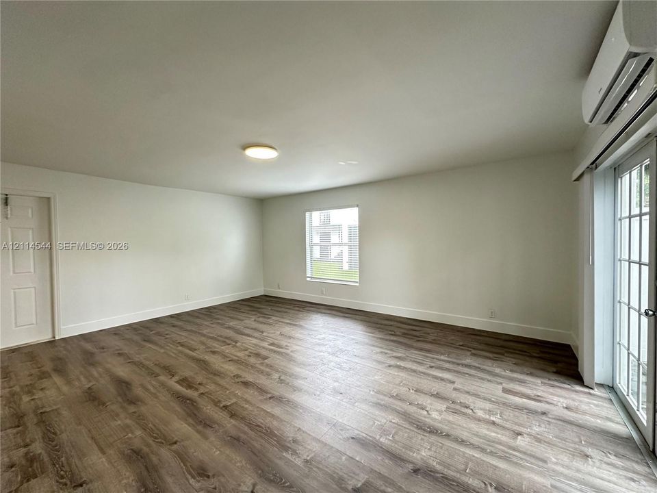Neutral-toned interior featuring wood-finish flooring, a wall-mounted ductless heating and cooling unit, flush-mount ceiling lighting, and a glass-paned exterior door