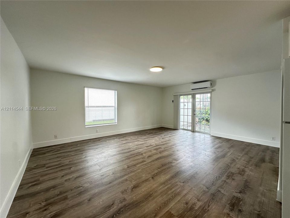 Open-concept interior featuring wood-finish flooring, a single-hung window with blinds, and glass-paned French doors