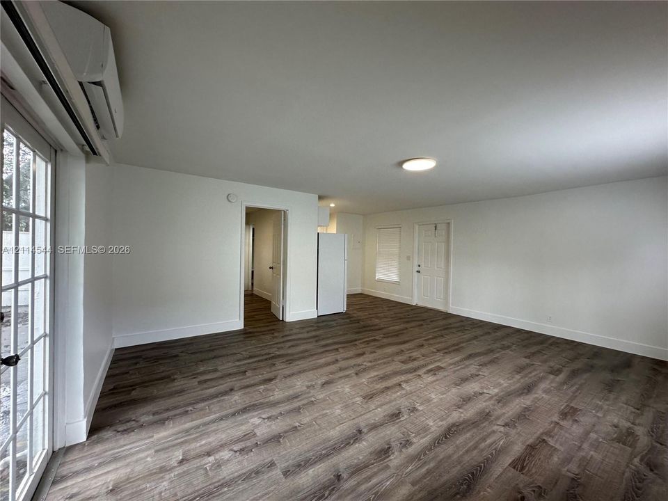 Open-concept interior featuring wood-finish flooring, a wall-mounted ductless heating and cooling unit, flush-mount ceiling lighting, and a multi-pane glass door