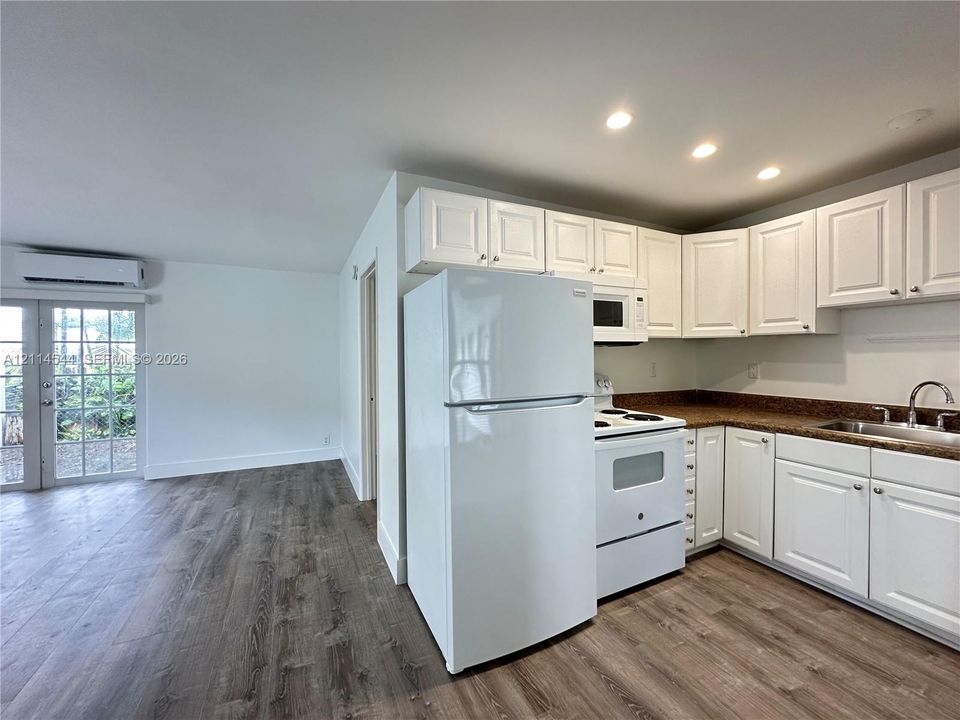 Kitchen featuring white shaker-style cabinetry, speckled countertops, stainless steel sink, wood-finish flooring, and glass-paneled patio door