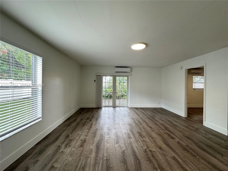 Wood-finish flooring, glass-paneled double doors, wall-mounted ductless air conditioning unit, and horizontal blind window treatments