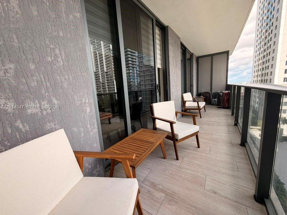 Covered balcony featuring textured wall finishes, full-height sliding glass doors, tile flooring, and a glass-paneled metal railing