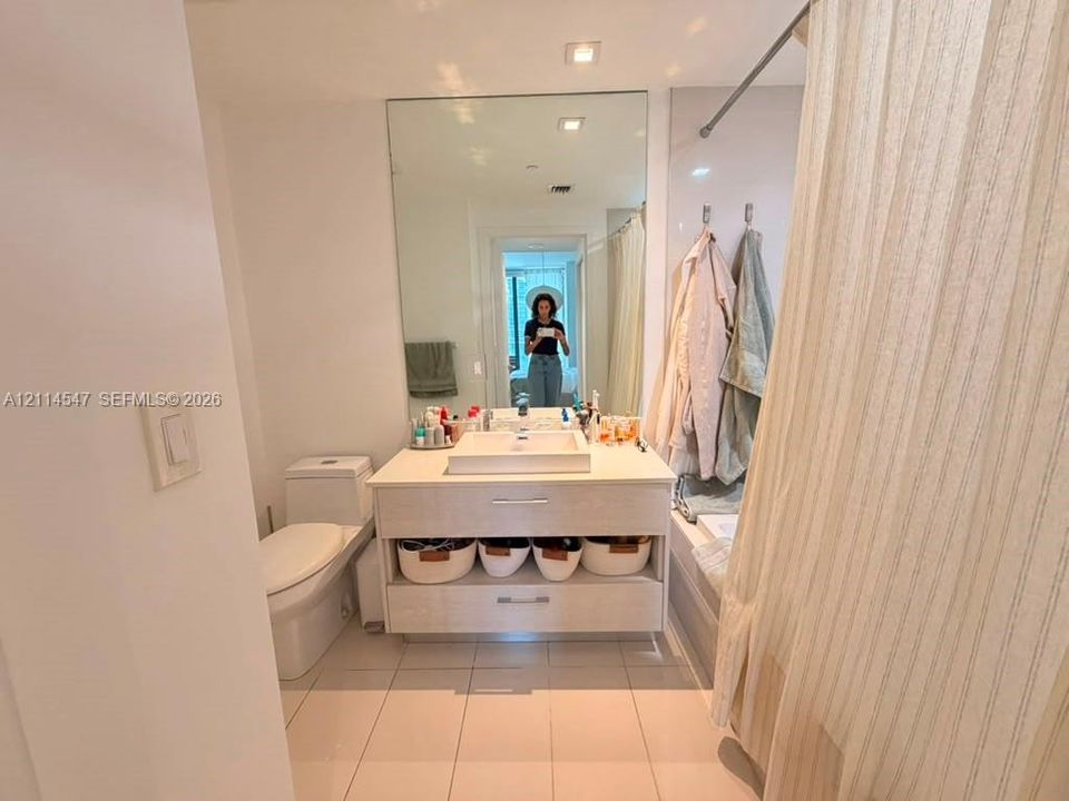 Bathroom vanity featuring a light wood-finish cabinetry, rectangular vessel sink, integrated storage shelf, full-height wall mirror, and porcelain tile flooring