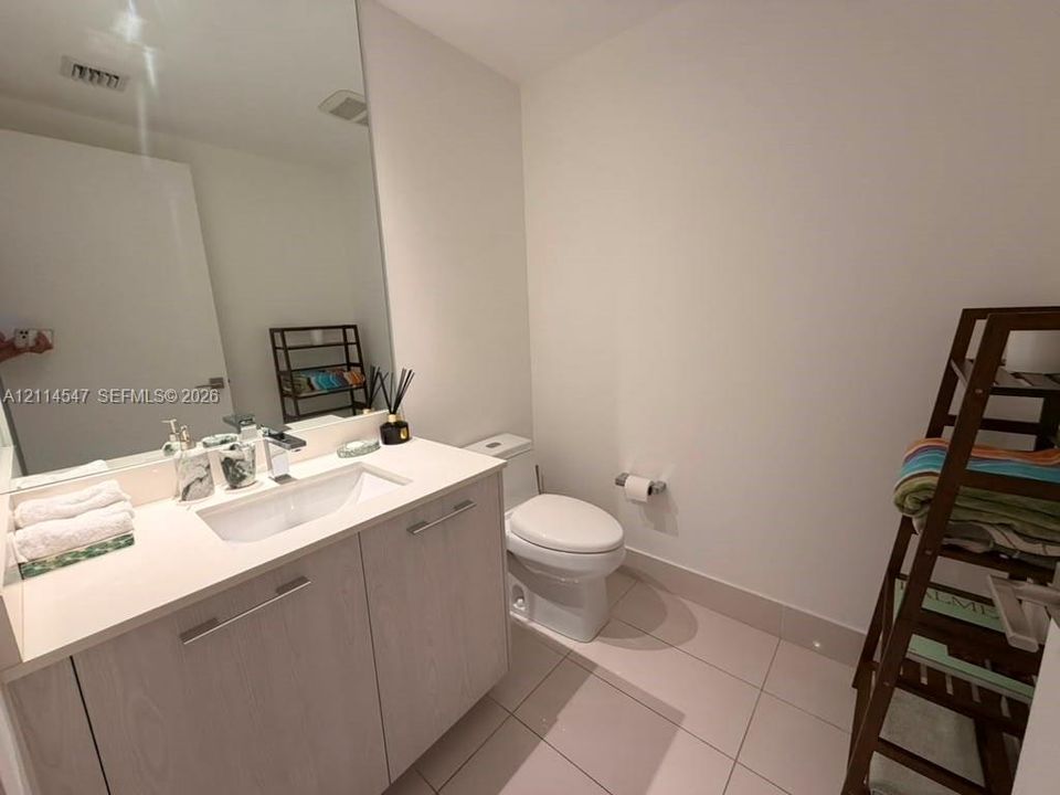 Bathroom featuring a light wood-finish vanity, solid-surface countertop with an integrated basin, large wall-mounted mirror, and tile flooring