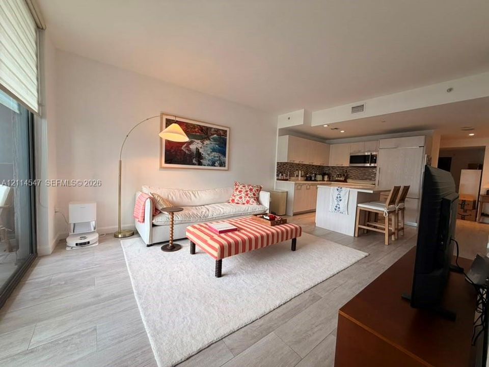 Open-concept floor plan featuring wood-finish flooring, kitchen island with built-in seating, flat-panel cabinetry, and floor-to-ceiling windows with roller shades
