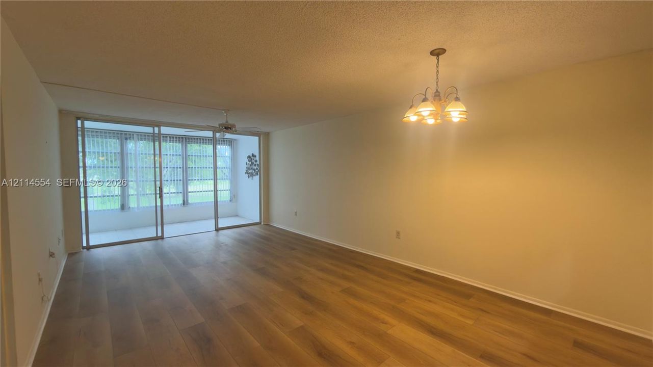 Open living area featuring wood-finish flooring, multi-light chandelier, ceiling fan, and sliding glass doors