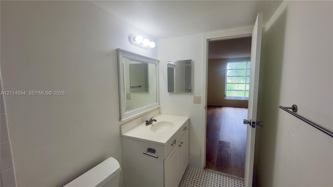 Bathroom vanity with integrated sink, framed wall mirror, three-light vanity fixture, and patterned tile flooring