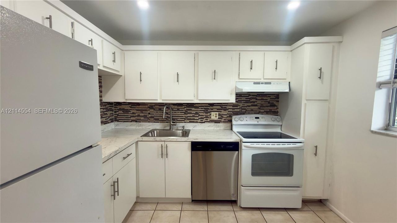 Kitchen featuring white shaker-style cabinetry, a multi-tone tile backsplash, stone-finish countertops, stainless steel dishwasher, and recessed ceiling lighting
