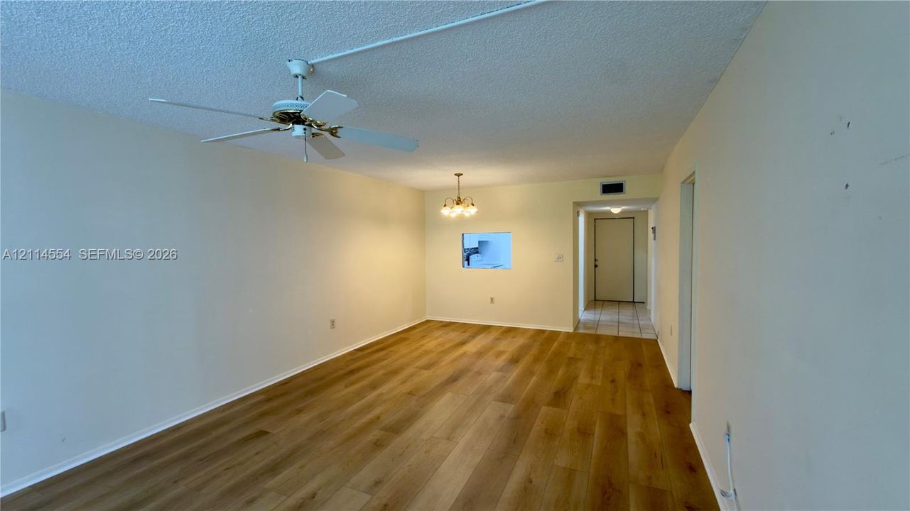 Open-concept interior featuring wood-finish flooring, a ceiling fan with integrated lighting, a multi-arm chandelier, and a decorative wall pass-through