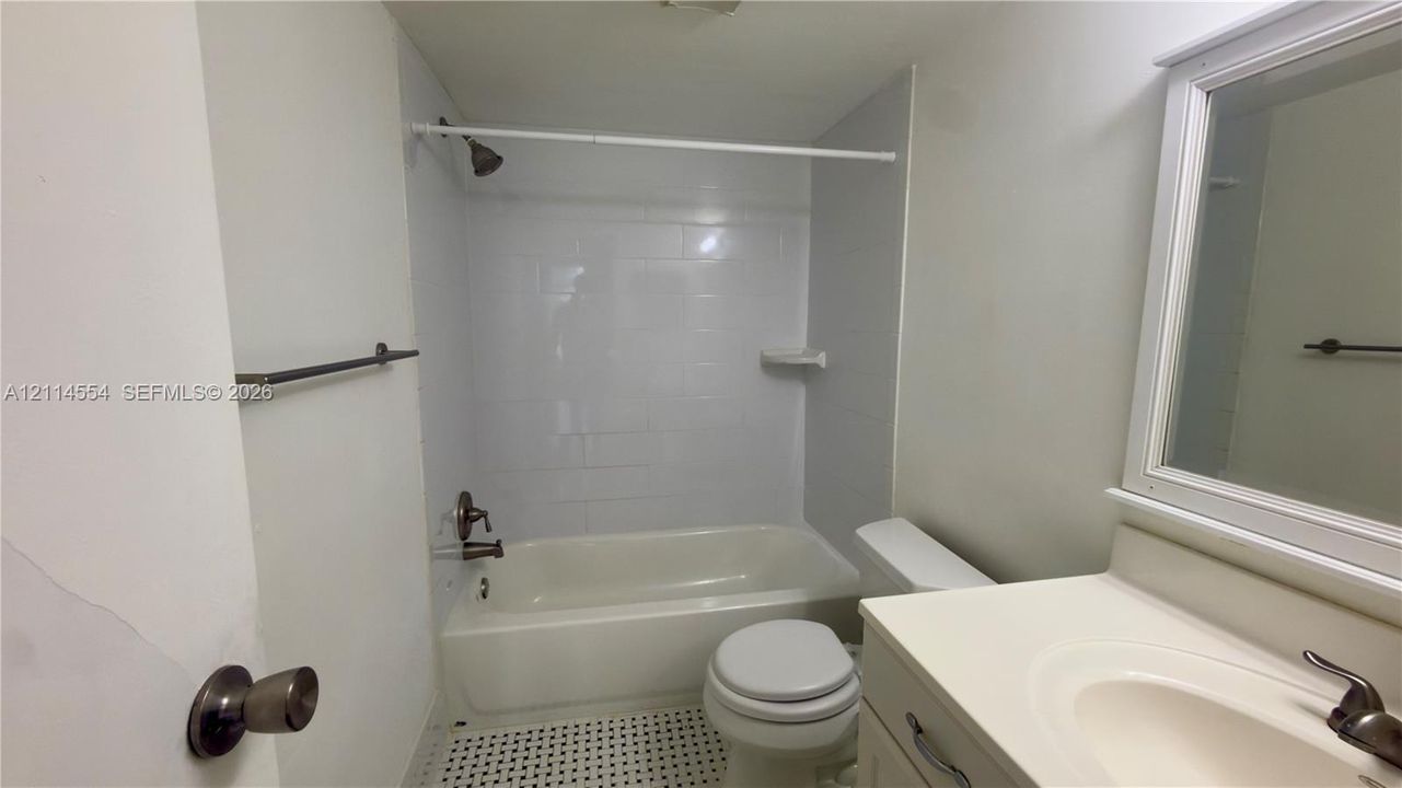 Bathroom featuring a white vanity with an integrated sink, shower-tub combination with white wall tile, and patterned tile flooring