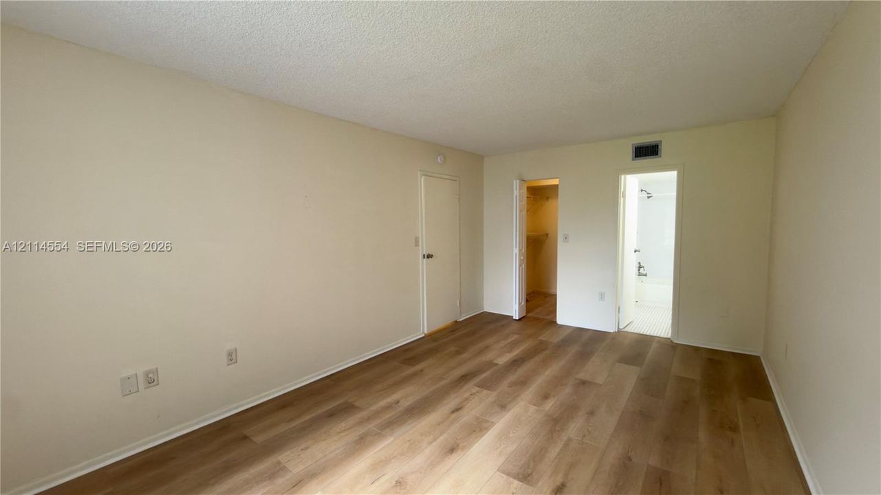Interior room featuring wood-finish flooring, neutral wall tones, a built-in closet with folding doors, and a doorway revealing a bathroom with a shower-tub combination
