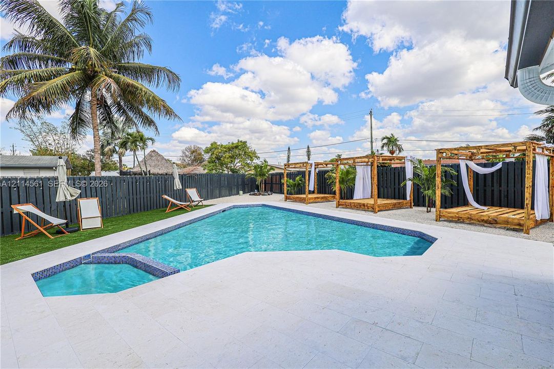In-ground pool featuring a tile-accented spa, light-toned stone pool deck, artificial turf, and a full-perimeter privacy fence